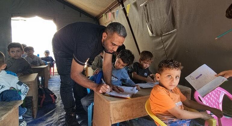 Un maestro ayuda a niños palestinos en un aula instalada en una tienda de campaña.